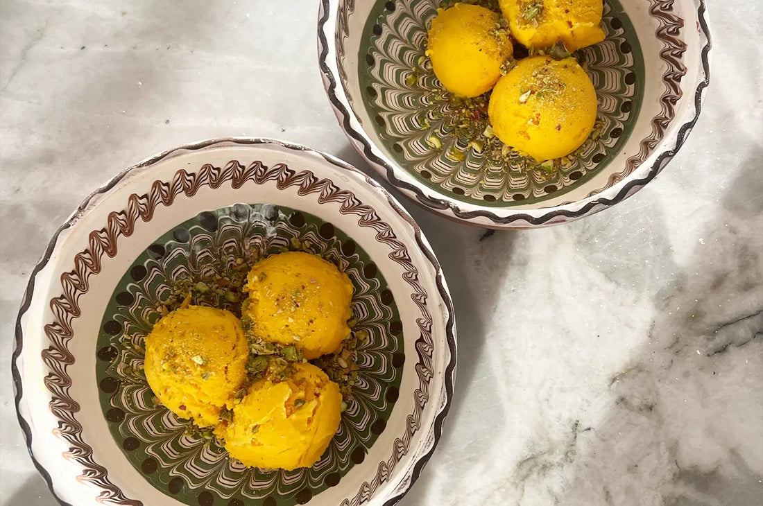 Close-up of a scoop of creamy saffron rose pistachio ice cream in a bowl, garnished with crushed pistachios and rose petals, evoking a fragrant, indulgent summer treat.