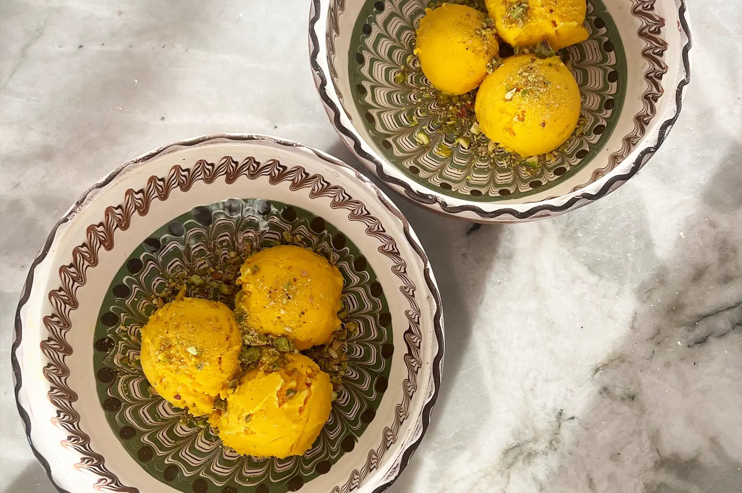 Close-up of a scoop of creamy saffron rose pistachio ice cream in a bowl, garnished with crushed pistachios and rose petals, evoking a fragrant, indulgent summer treat.