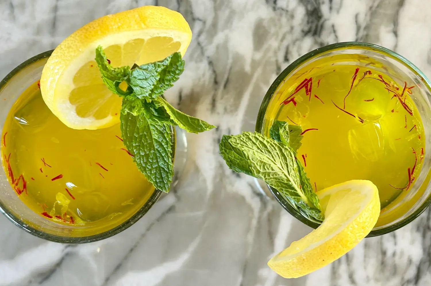 "Glass of vibrant saffron summer mocktail garnished with fresh herbs, set against a sunlit backdrop—a refreshing, alcohol-free wellness drink."