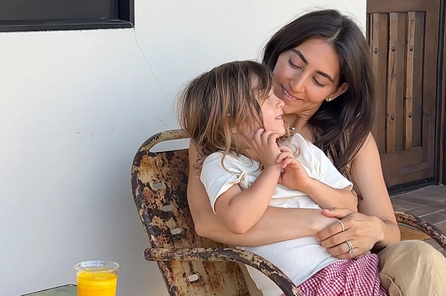 Nikki sitting with her daughter hugging her closely on a sunny summer day, both sharing a tender moment with a saffron latte placed nearby, surrounded by warm light and relaxed, homey vibes.