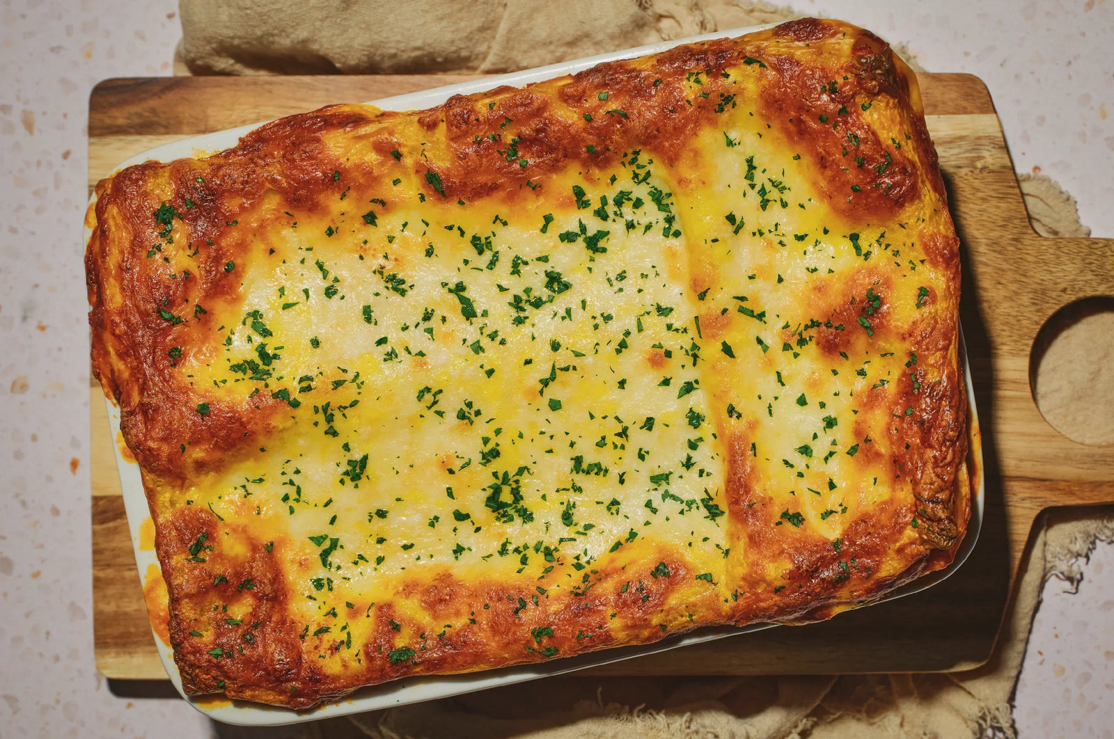 Saffron Lasagna with fresh herbs, melted cheeses over a cutting board 