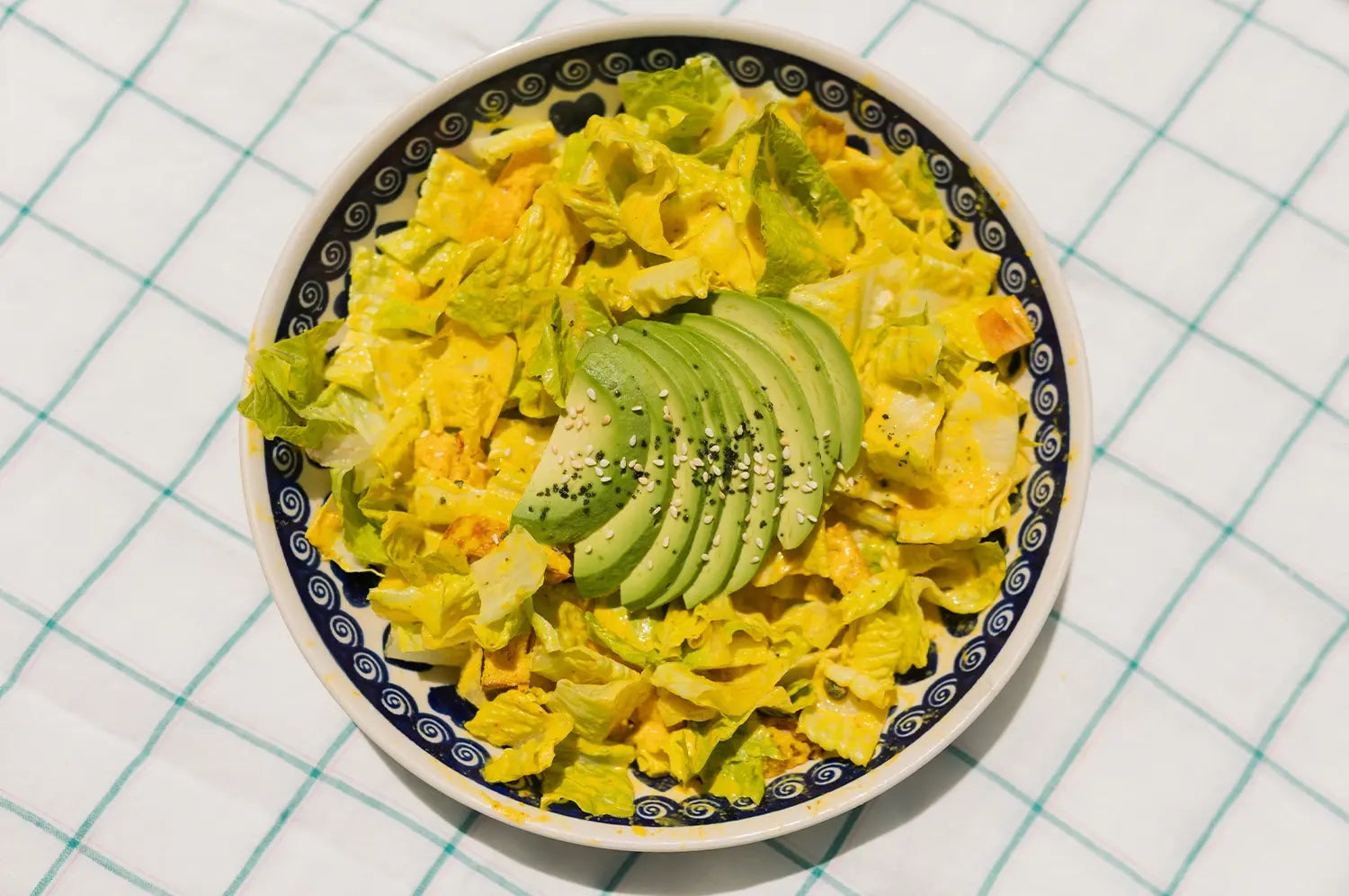 A vibrant Caesar-style salad tossed with saffron tahini dressing, topped with crunchy chickpeas and herbs, served in a ceramic bowl on a light, sunlit table with Mediterranean-inspired decor.