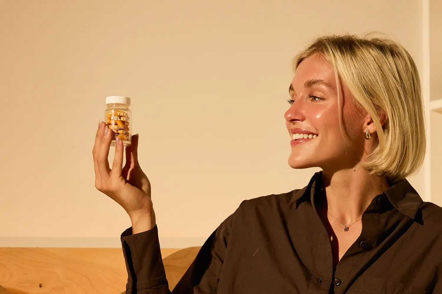 Young woman smiling at a bottle of saffron capsules with a neutral background 