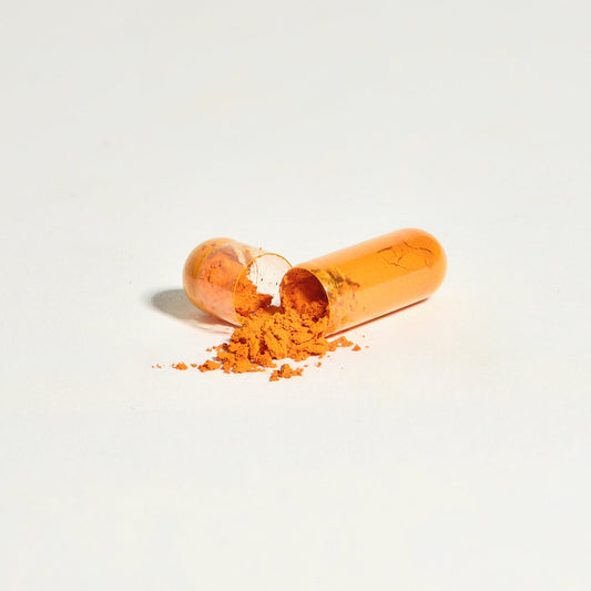 A translucent Saffron Capsules by THE FULLEST pulled apart, revealing orange powder spilling onto a white surface for mood support.