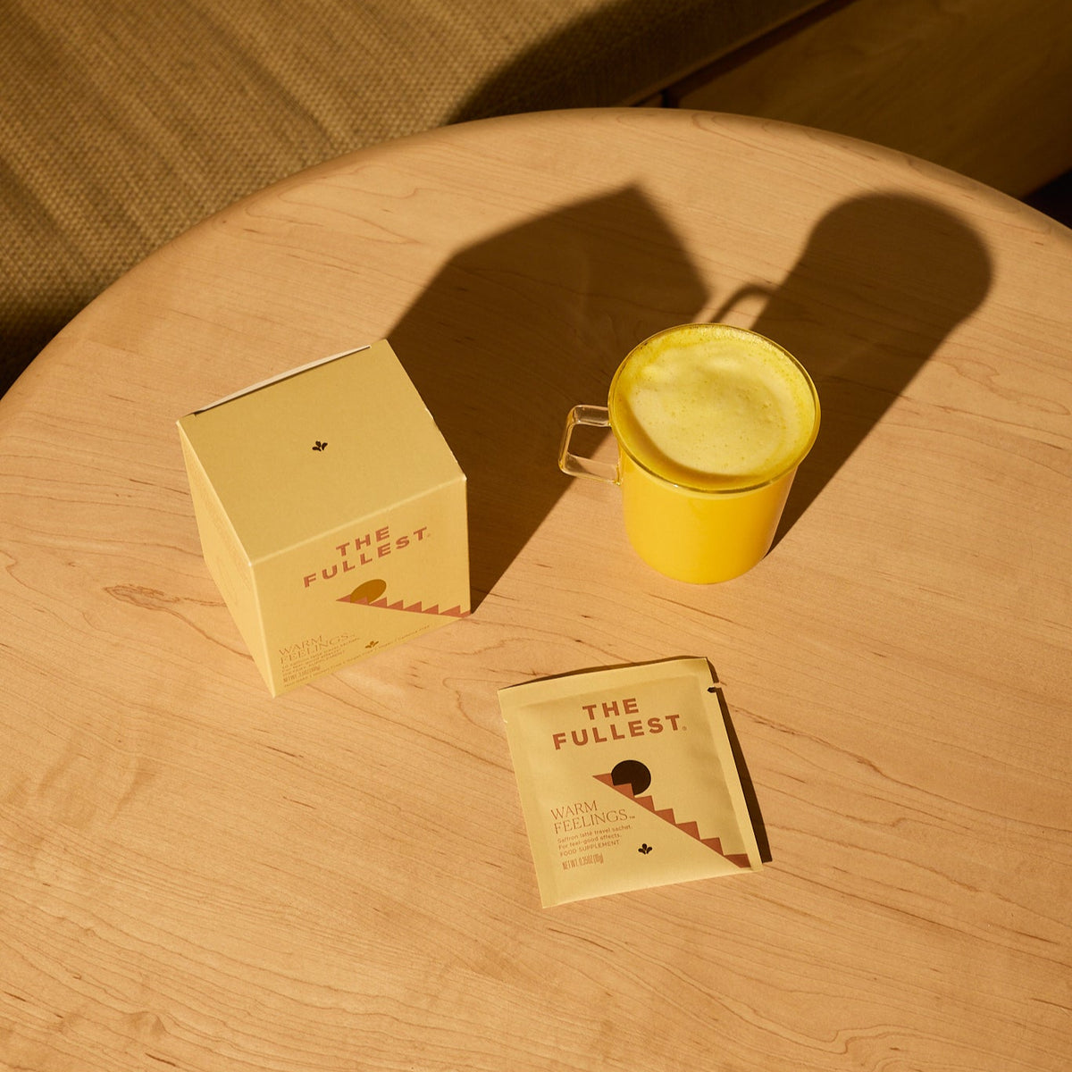 Round wooden table with a yellow mug, box, and sachet on a couch background