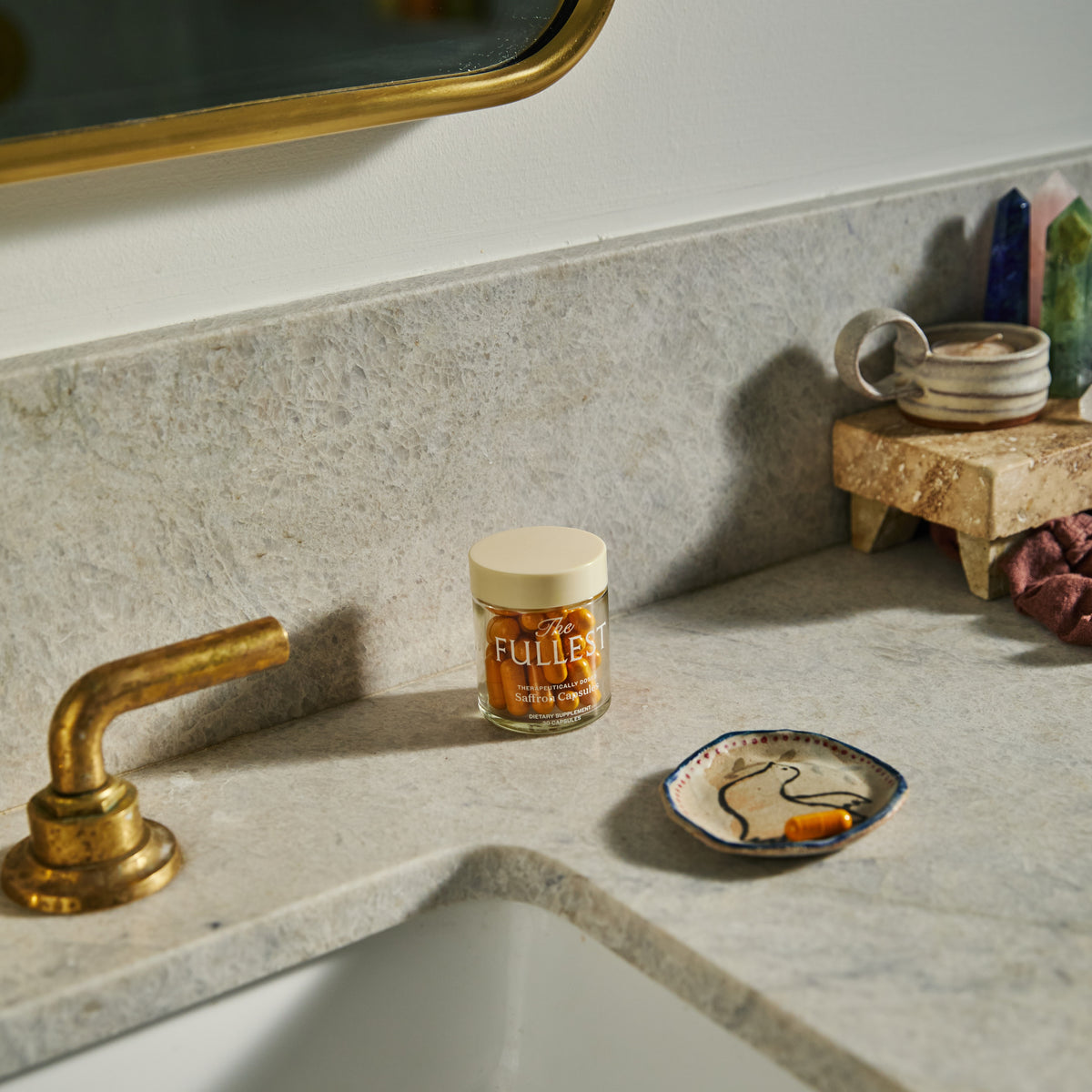 A glass bottle of THE FULLEST Saffron Capsules and a single loose capsule on a small decorative dish next to a bathroom sink.