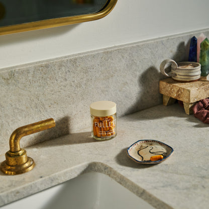 A glass bottle of THE FULLEST Saffron Capsules and a single loose capsule on a small decorative dish next to a bathroom sink.