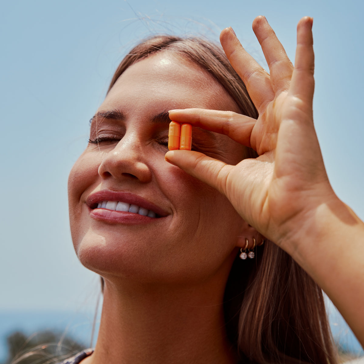A person with eyes closed holds two orange THE FULLEST Saffron Capsules for mood support between their thumb and forefinger in front of their face.