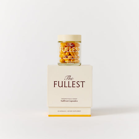 A glass jar of THE FULLEST Saffron Capsules resting on a matching cream-colored box for mood support.