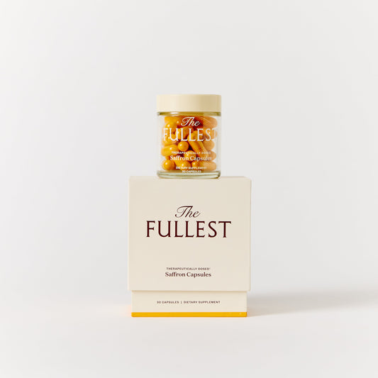 A glass jar of THE FULLEST Saffron Capsules resting on a matching cream-colored box for mood support.