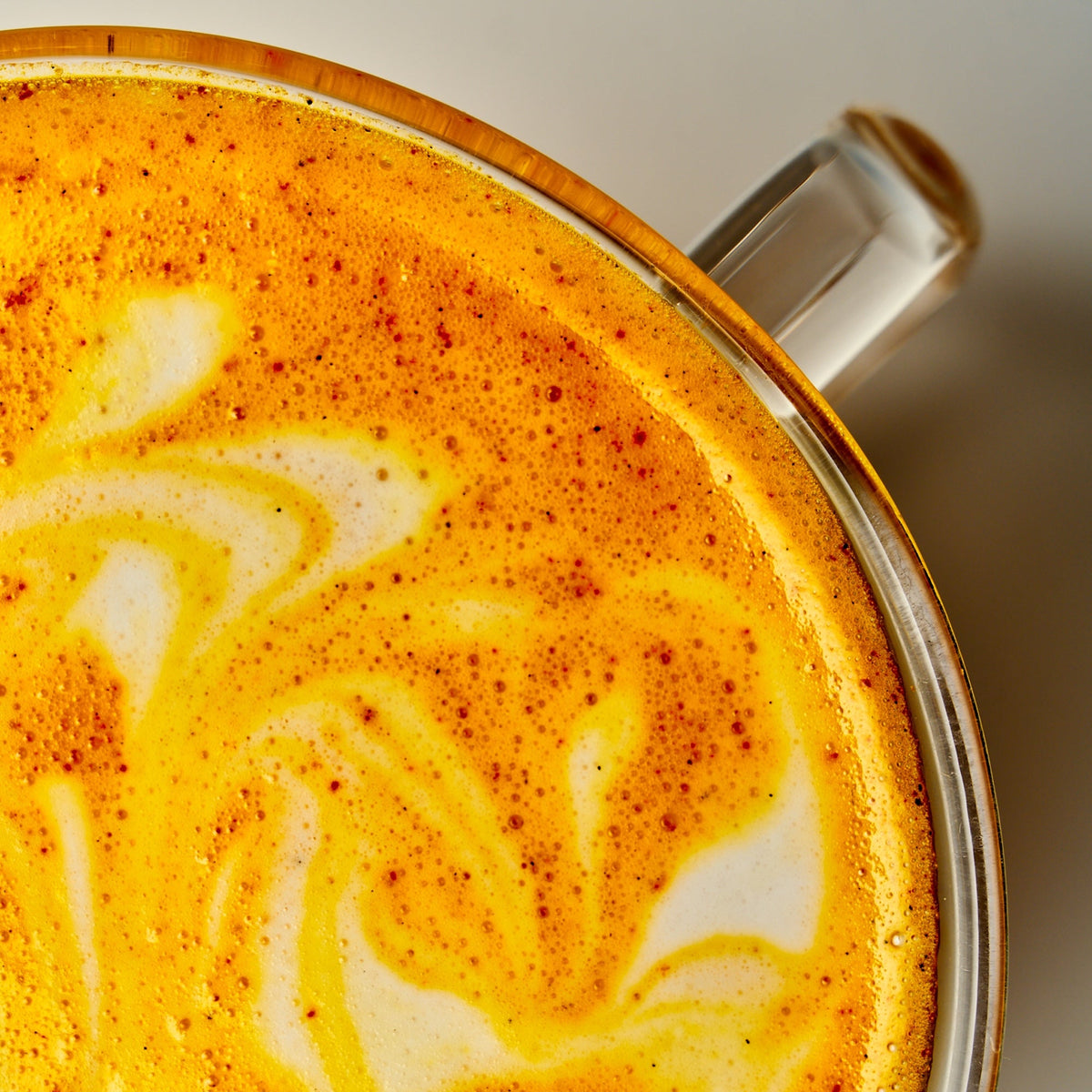 A top-down, close-up view of a bright yellow Saffron latte in a clear glass mug with a swirl pattern in the foam.