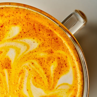 A top-down, close-up view of a bright yellow Saffron latte in a clear glass mug with a swirl pattern in the foam.