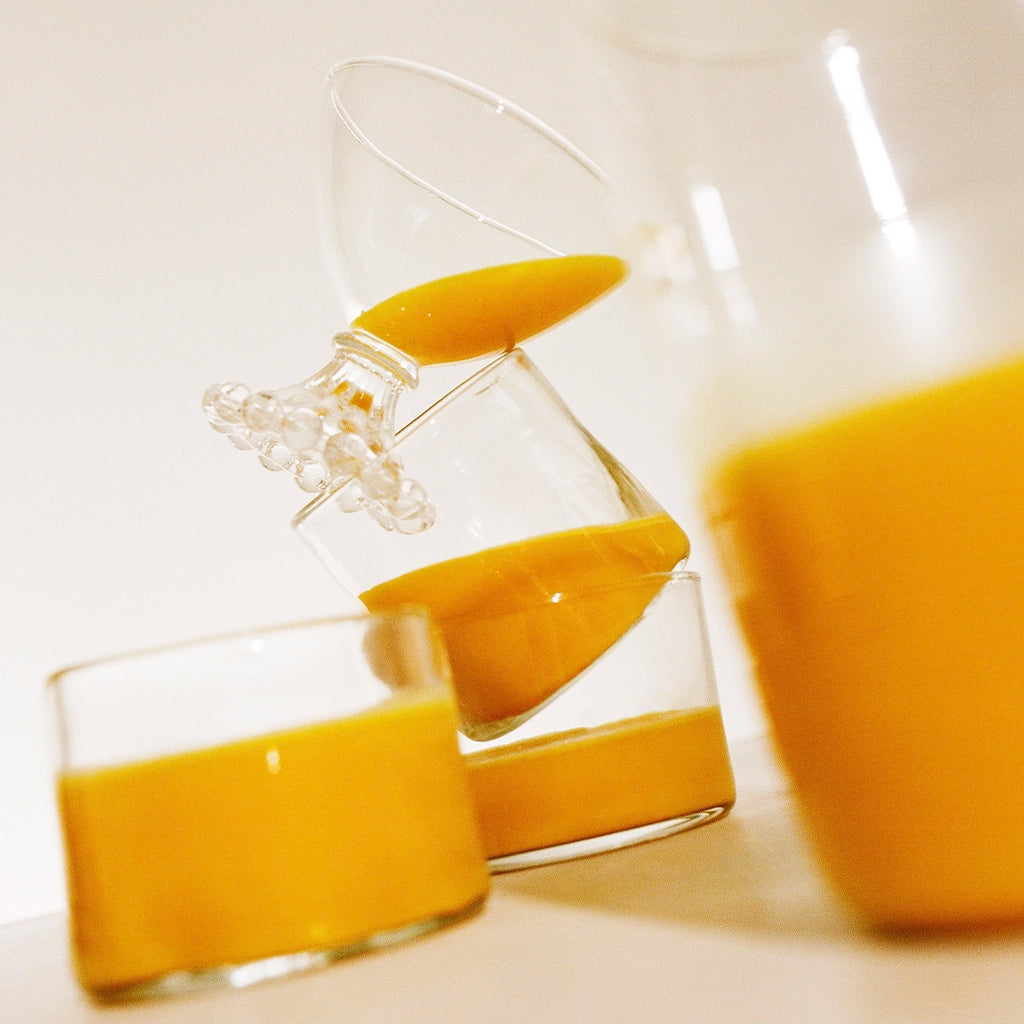 Close-up of saffron beverage being poured from a glass jug into a glass, with another full glass visible in the foreground.