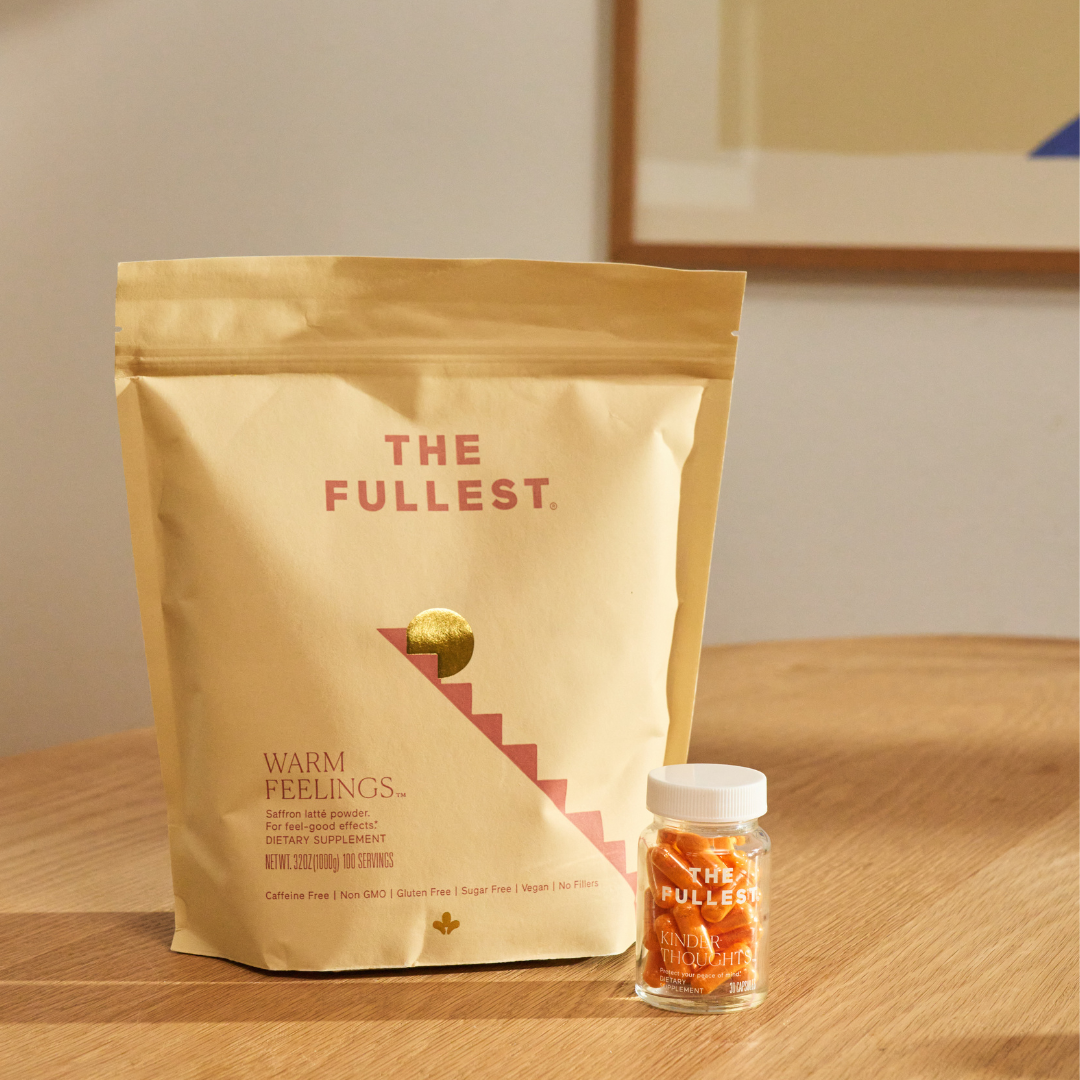 A beige pouch labeled "THE FULLEST." and a small clear bottle of orange-colored saffron capsules rest on a wooden table in a softly lit room.