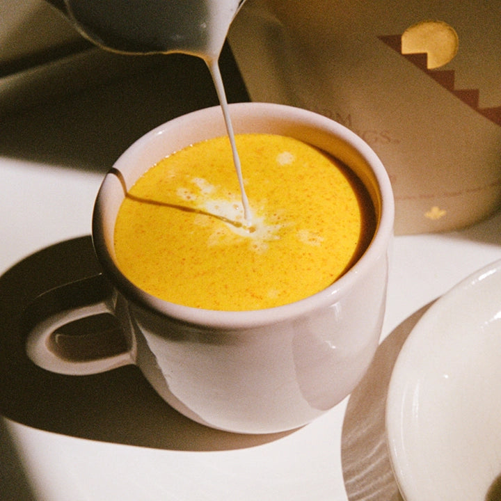 A pitcher of steamed milk being poured into a mug of THE FULLEST Warm Feelings saffron latte.