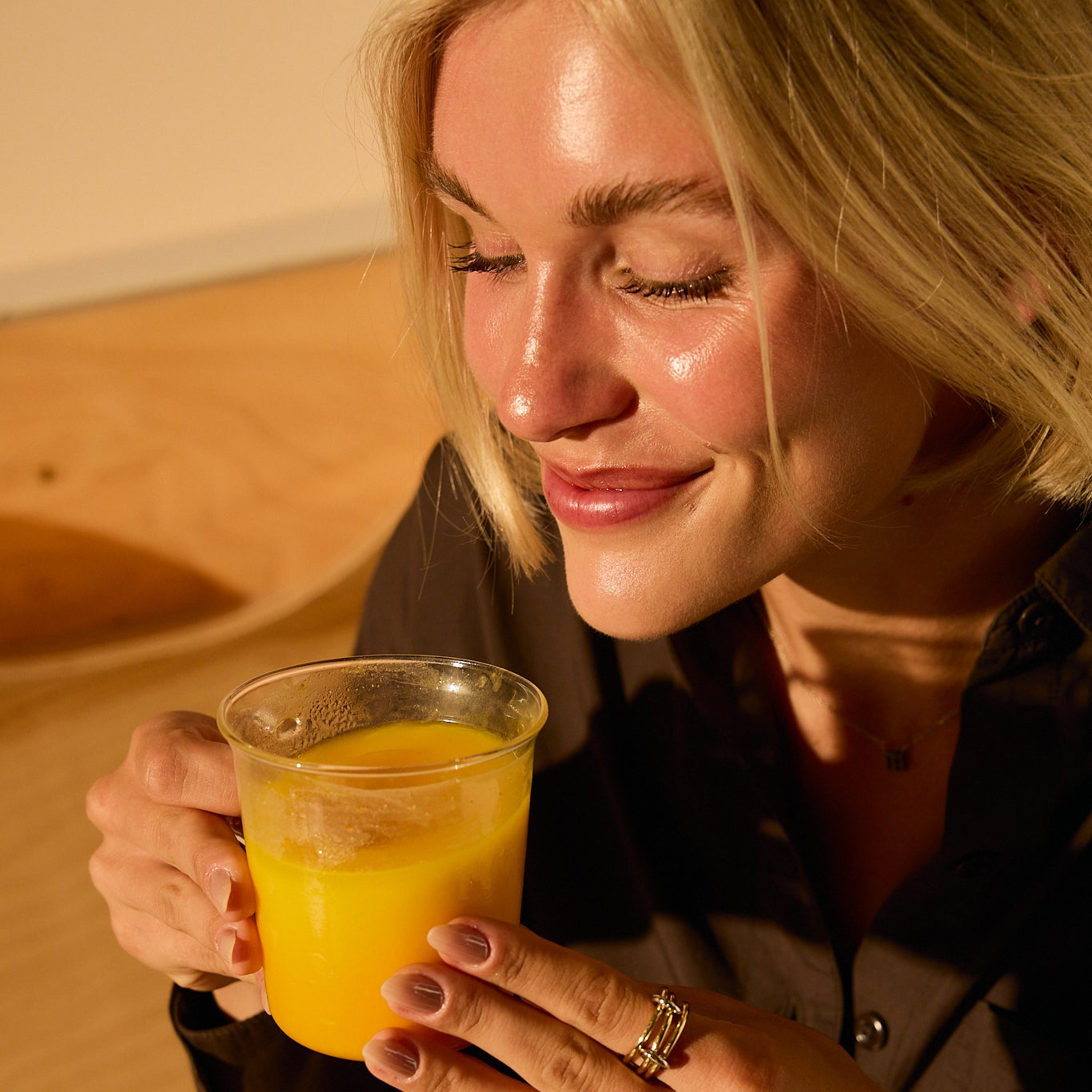 A woman with blonde hair smiles with closed eyes, enjoying a caffeine-free mood boost as she holds a cup of THE FULLEST Saffron Latte in warm, natural light.