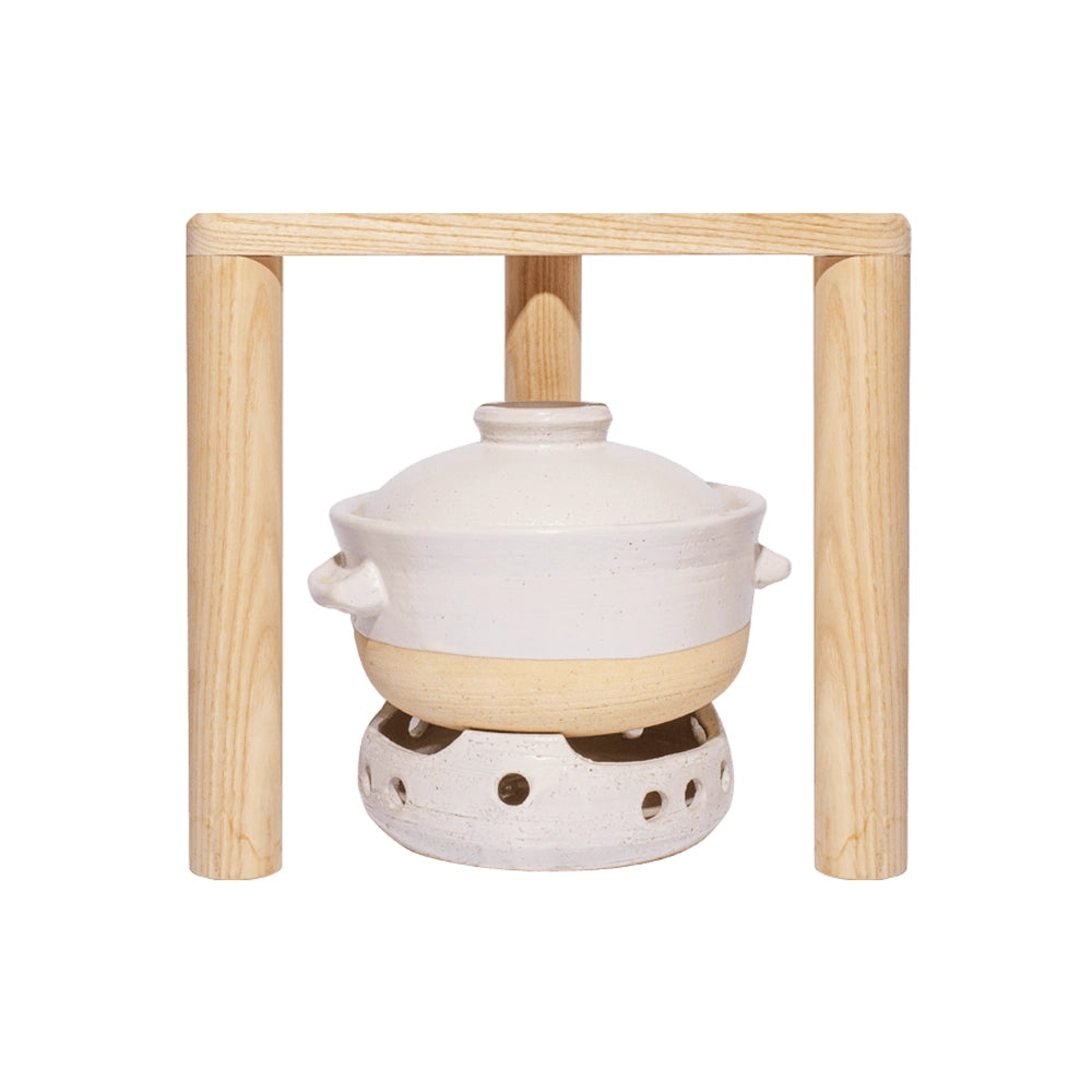 A white ceramic Womb Protector Ritual Bundle fondue pot with handles, placed on a wooden stand with a tealight holder underneath, isolated on a white background.
