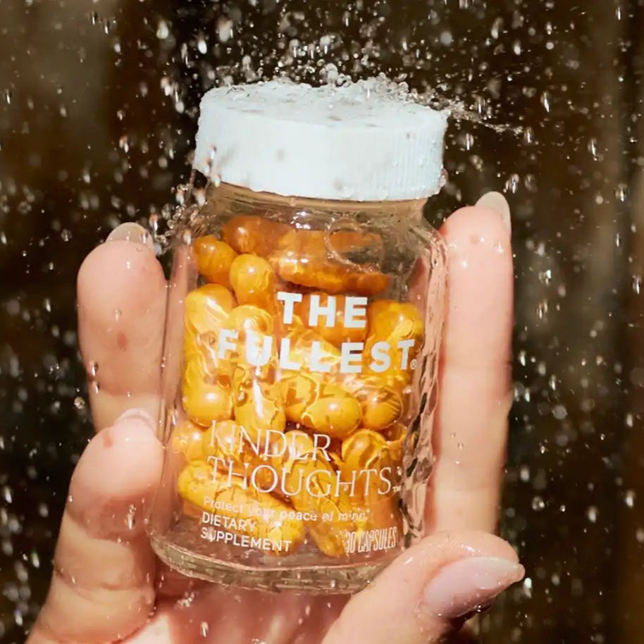 A hand holds a bottle of THE FULLEST Saffron capsules as water splashes over the lid.