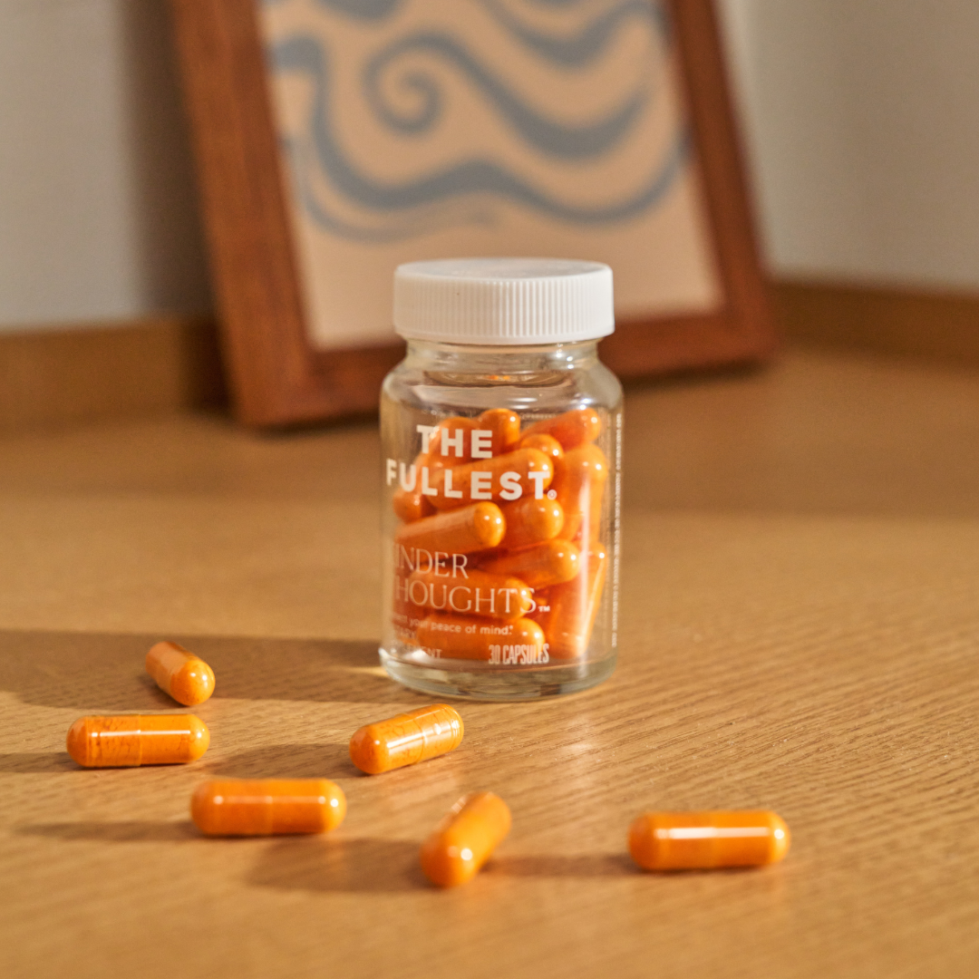 A clear jar labeled "THE FULLEST Saffron Capsules" sits on a wooden surface, filled with saffron capsules and several capsules scattered nearby.