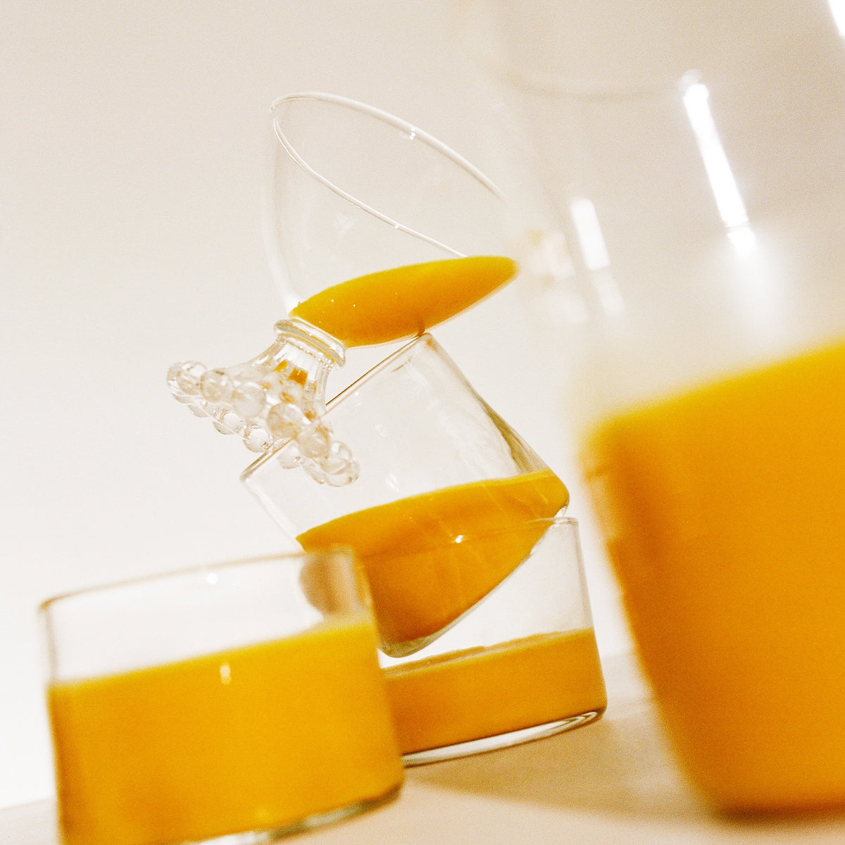 A carafe and three glasses of a saffron infused beverage with a dynamic pour in motion by THE FULLEST.